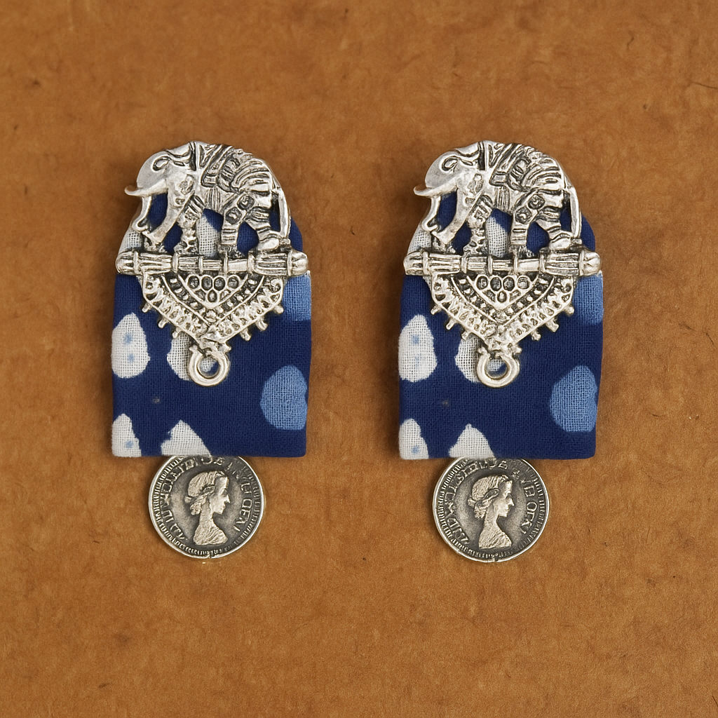 Pair of silver elephant earrings with blue polka dot fabric on a brown background