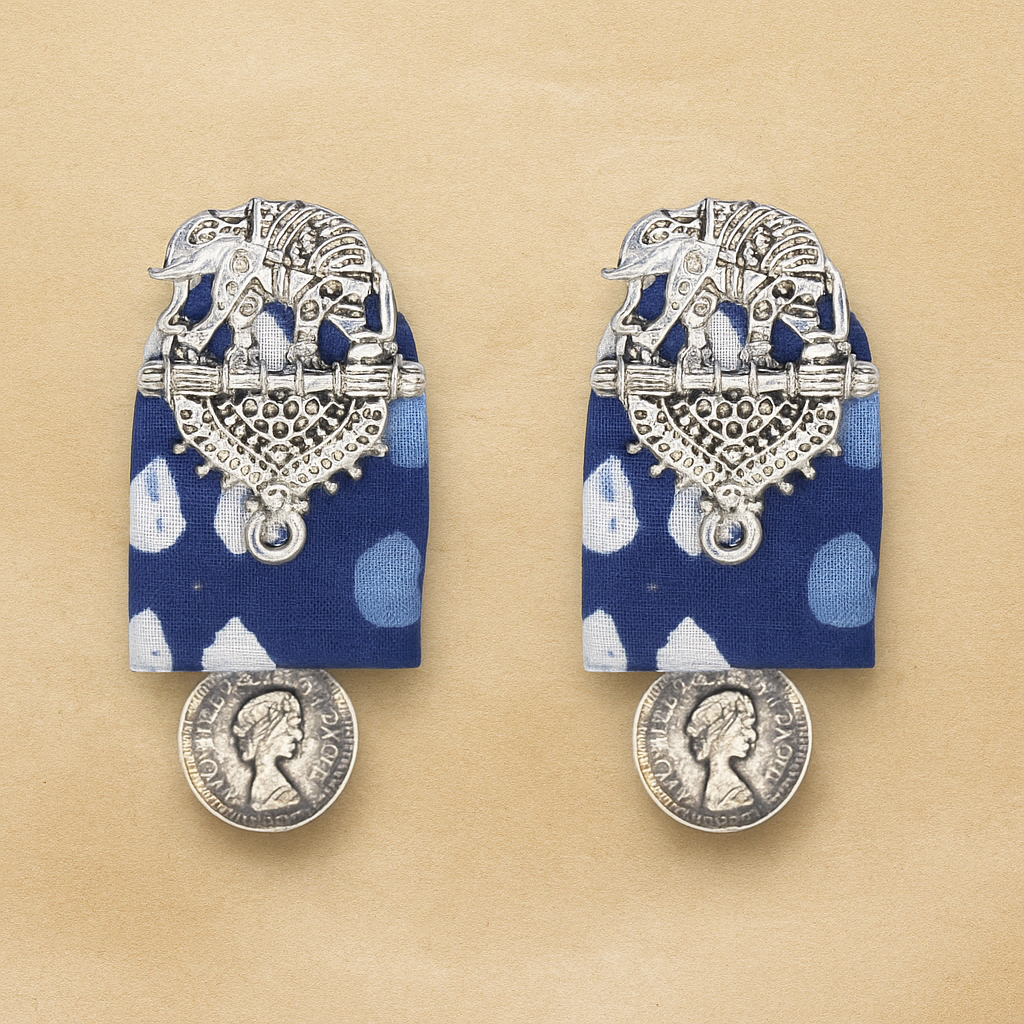 Pair of hand crafted earrings with indian silver elephant decorative tops on Blue indigo fabric and silver coin-like bottoms on a beige background