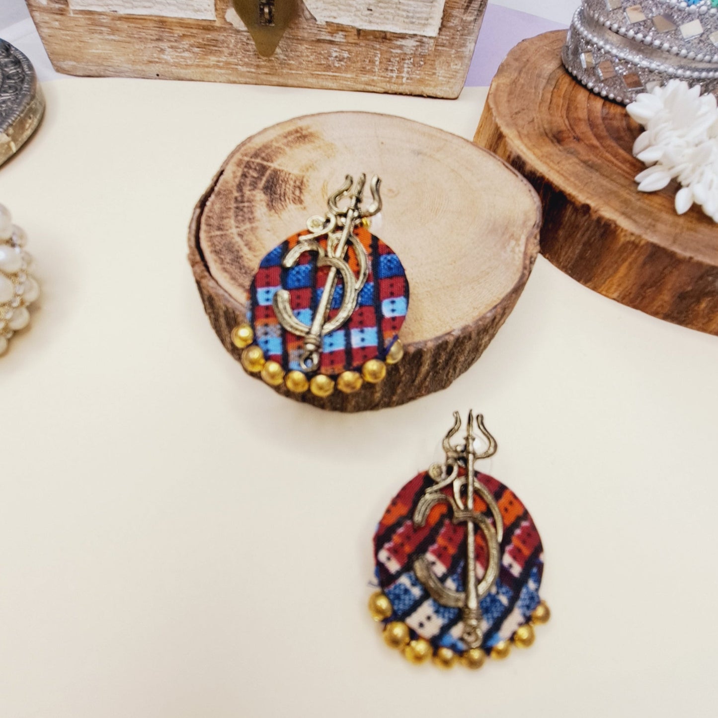 A pair of multicolored fabric earrings with golden studs and om and trishul designs displayed on a wooden stand.