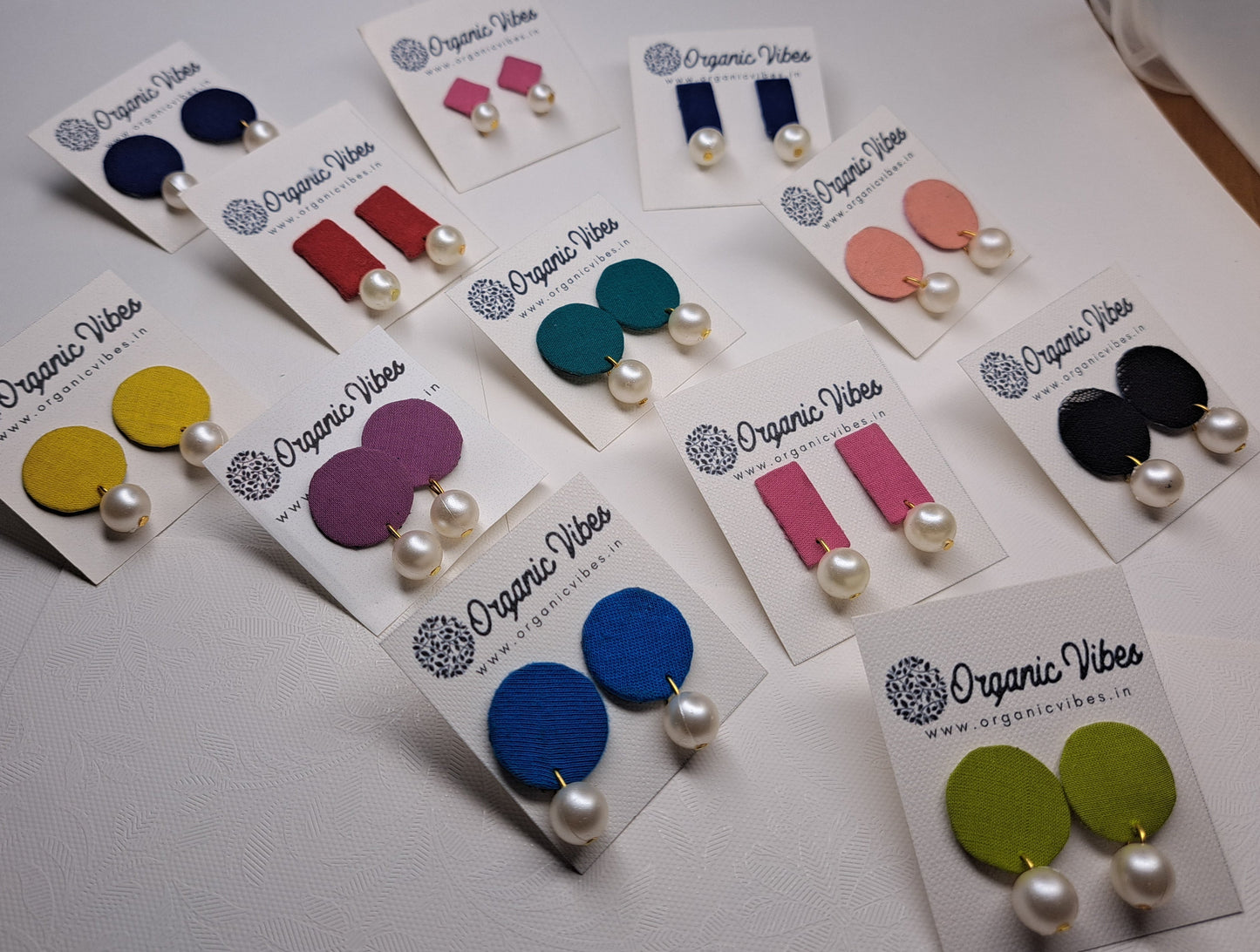 Colorful assorted fabric and pearl earrings on cards with 'Organic Vibes' branding on a white surface.