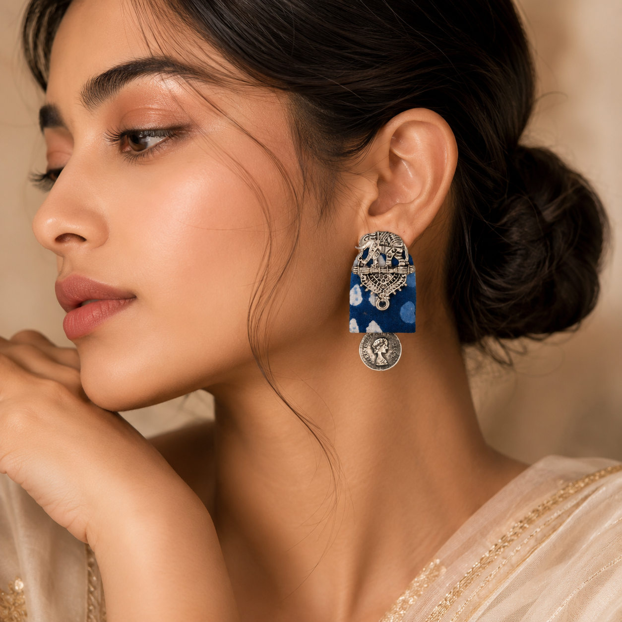 A close-up lifestyle shot of a woman wearing a pair of ornate blue and silver earrings. The earrings feature intricate silver filigree work, a blue rectangular panel with white floral patterns, and a dangling silver coin charm.