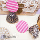 A pair of handmade fabric earrings with a pink and white striped pattern and silver jhumka design, displayed against a wooden background with decorative elements.