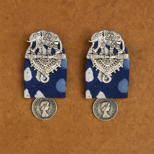 Pair of silver elephant earrings with blue polka dot fabric on a brown background