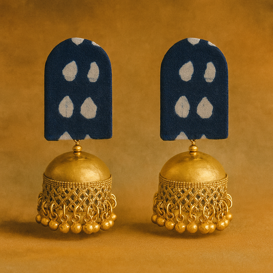 Pair of gold jhumka earrings with blue and white stone-studded pendants on a brown background