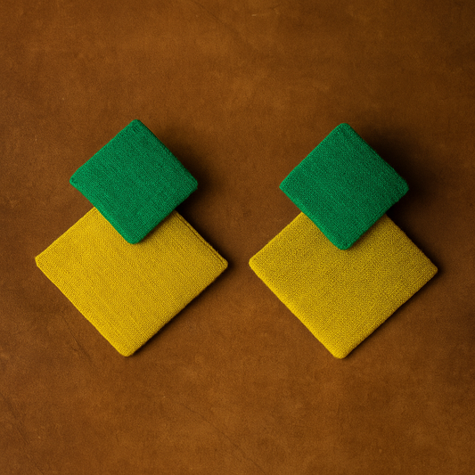 Pair of fabric earrings with green and yellow square designs on a brown background