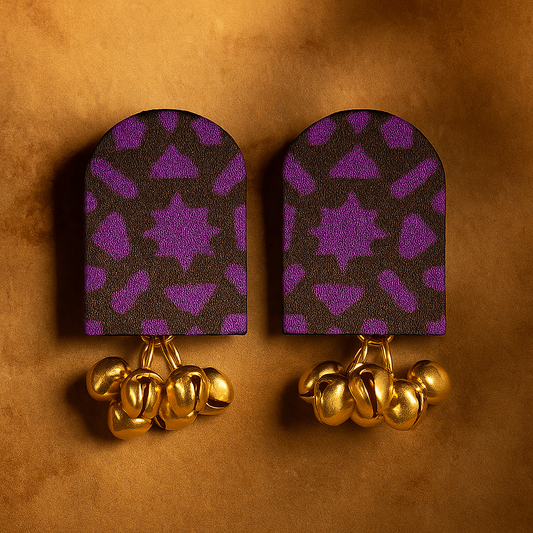 Pair of  fabric earrings with purple patterned backs and gold accents on a brown background
