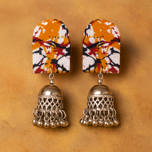 Pair of earrings with floral fabric and silver jhumka design on a brown background