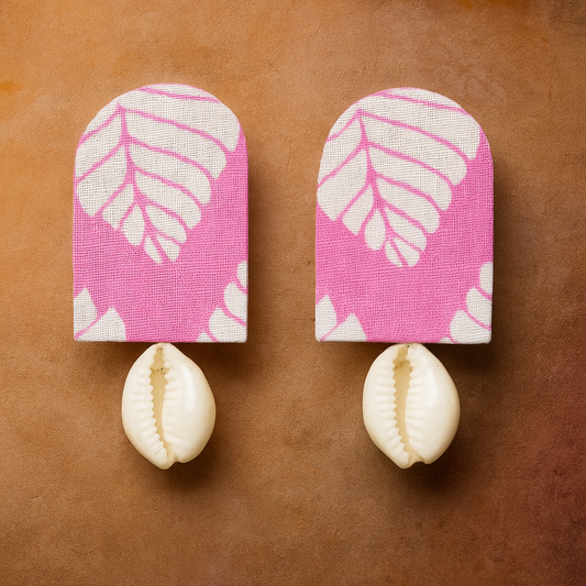 Two fabric wall hooks with pink and white leaf pattern and cowrie shells on a brown background