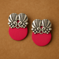 Pair of earrings with silver floral designs on red circular pendants against a brown background